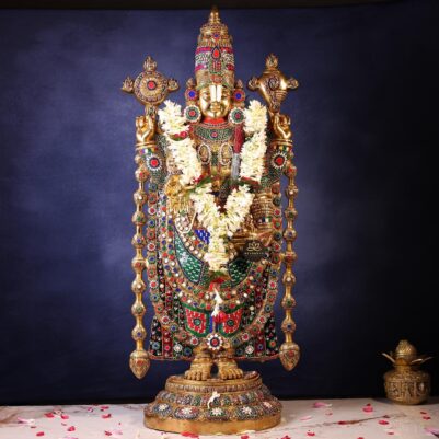 Intricate multicolored gem detailing on brass idol adorned with white flower garlands standing tall