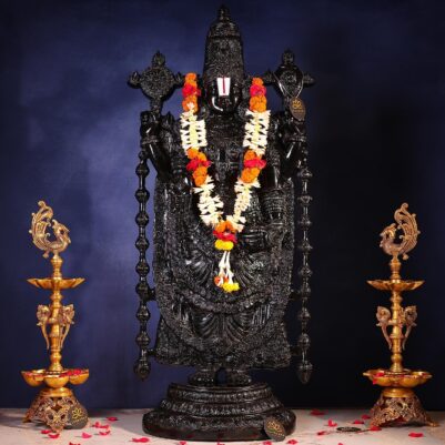 Front view of black stone tirupati balaji idol adorned with floral garland and traditional lamps